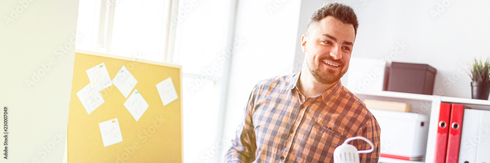 The man is standing in the office near the board with stickers and is leading a besside. The man is standing in the office near the board with stickers and is leading a besside.