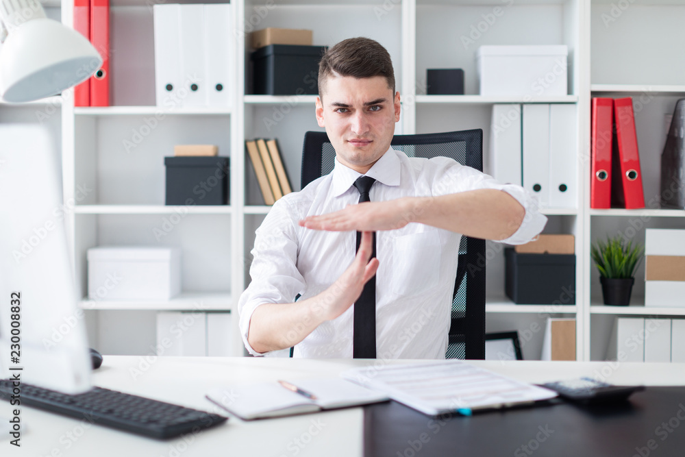 Fototapeta premium The young man is sitting at a computer Desk in the office and put his hands perpendicular to each other.