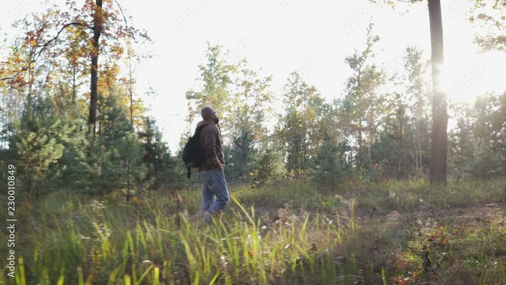 A handsome, bearded young man with a backpack on his back walks through the forest, breathes fresh air and enjoys the autumn landscape. Through the trees the sun A handsome, bearded young man with a backpack on his back walks through the forest, breathes fresh air and enjoys the autumn landscape. Through the trees the sun