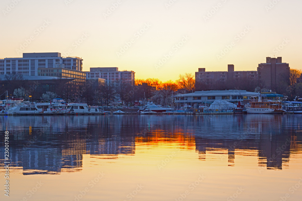 Yachts and urban buildings reflections during cherry blossom season in Washington DC. East Potomac Washington channel at sunrise.