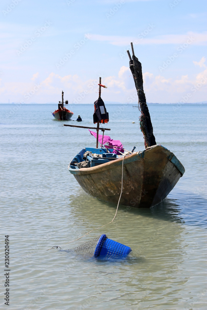 A small traditional wooden Asian fishing boat moored in a bay with a  fisherman working in the ocean silhouetted in the background. Stock Photo