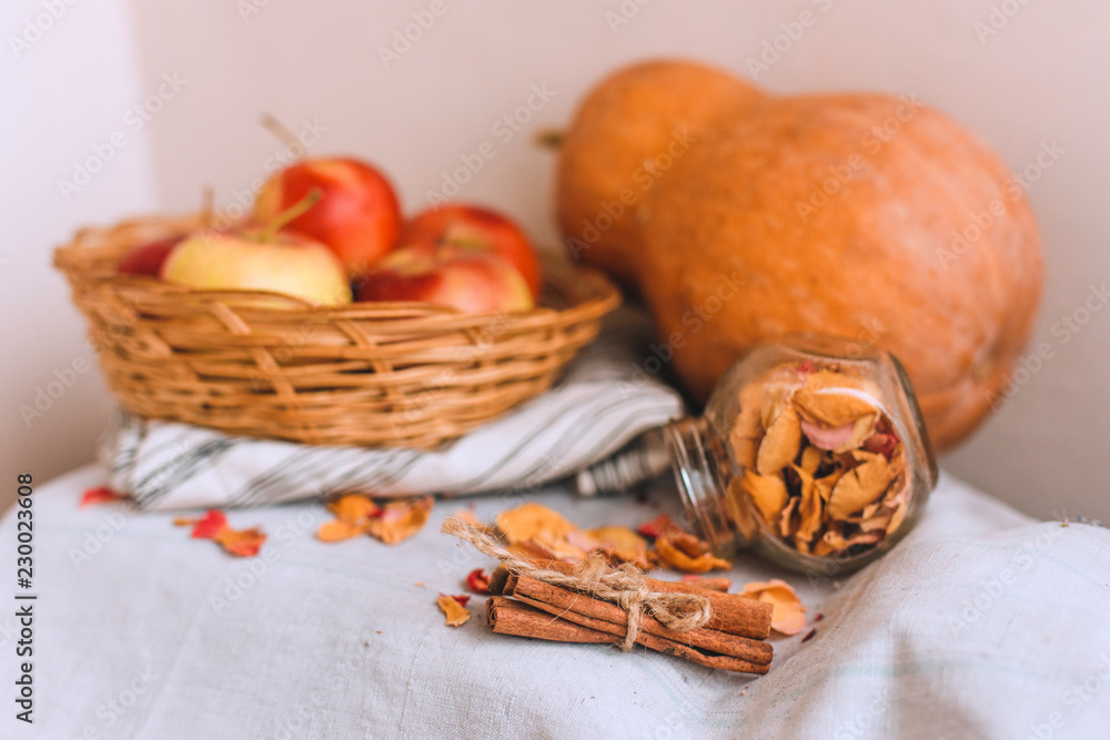Still life with cinnamon sticks wrapped in twine, apples in a wicker basket stand on a striped linen cloth, walnuts and flower petals. Concept of home comfort in autumn or winter. Still life with cinnamon sticks wrapped in twine, apples in a wicker basket stand on a striped linen cloth, walnuts and flower petals. Concept of home comfort in autumn or winter.