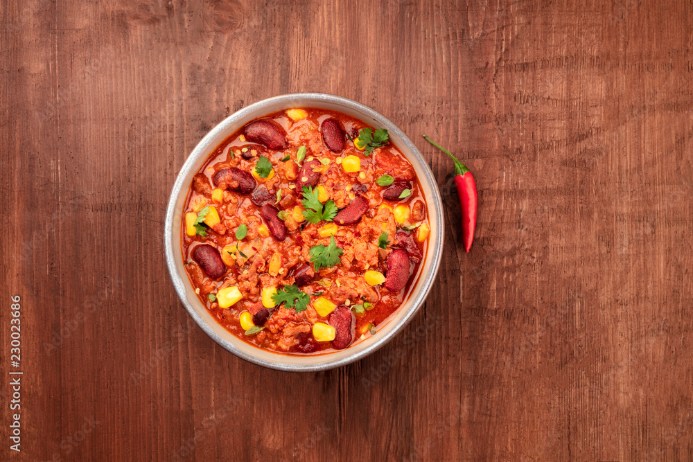 Chili con carne, traditional Mexican dish, with a chilli pepper, shot from above on a dark rustic wooden background with copy space Chili con carne, traditional Mexican dish, with a chilli pepper, shot from above on a dark rustic wooden background with copy space