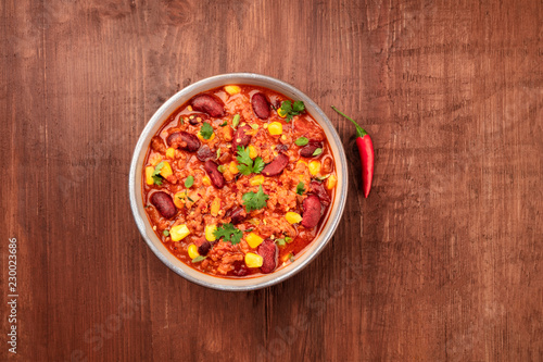 Chili con carne, traditional Mexican dish, with a chilli pepper, shot from above on a dark rustic wooden background with copy space