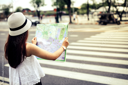 Young woman wearing a hat is looking at a map to walk along the streets, She is looking for attractions in asian country.
