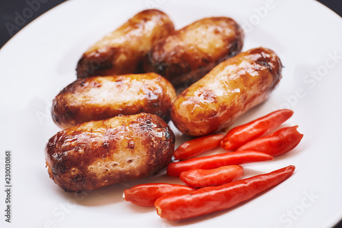 Thai food, pork sausage grilled with red chilies on white plate.