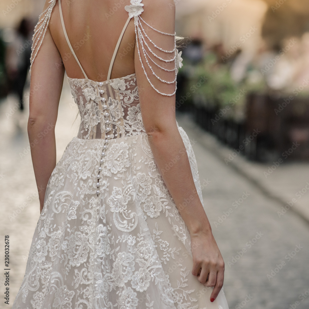 Bride in white silk dress with lace standing back on city street