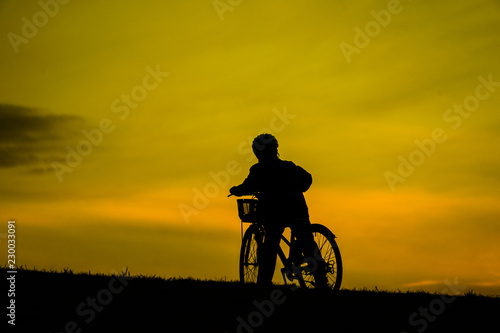 日没の丘で自転車に乗る少年