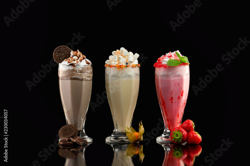 Fotografia Three glasses of colorful milkshake cocktails - chocolate, strawberry and vanilla decorated with fresh berries and mint isolated at black background