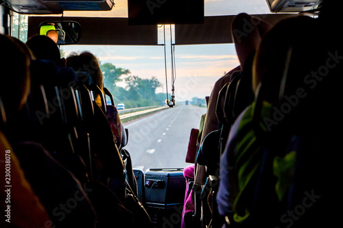 Saloon of bus with passengers. The light of the sun penetrates through the windshield of the bus. From the window of the tourist bus you can see the road_