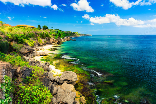 Fototapeta Naklejka Na Ścianę i Meble -  Azure beach with rocky mountains and clear water of Indian ocean at sunny day / A view of a cliff in Bali Indonesia / Bali, Indonesia