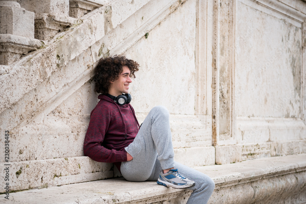 Handsome young man with headphones around his neck relaxing in front of stone wall Handsome young man with headphones around his neck relaxing in front of stone wall