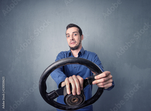 Young man holding black steering wheel on a blueish gray background