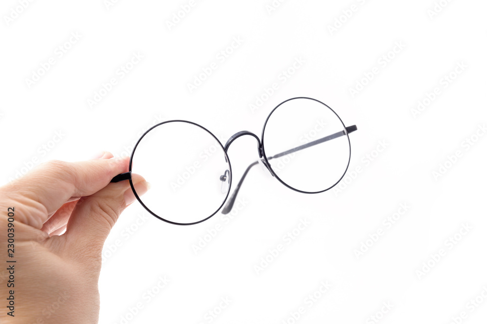 Round black-rimmed glasses are located frontally, Hand holds glasses. Isolated on a light background. Round black-rimmed glasses are located frontally, Hand holds glasses. Isolated on a light background.