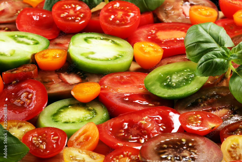various colorful tomatoes and basil leaves on rustic table.