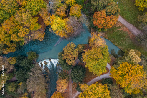 Herbstlich, farbenfroh leuchtende Bäume im Herbst von oben aus der Vogelperspektive an einem kleinen See oder Fluß als Drohnenshot