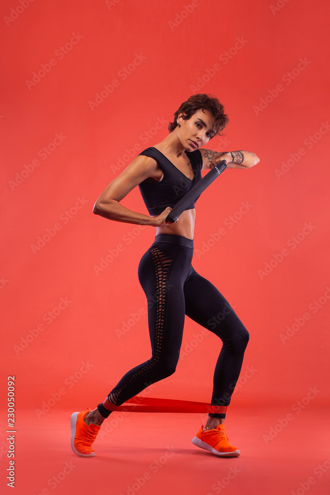 Fitness and sport motivation.. Strong and fit athletic, woman with tattoo posing on red background in sportswear. Fitness and sport motivation.. Strong and fit athletic, woman with tattoo posing on red background in sportswear.
