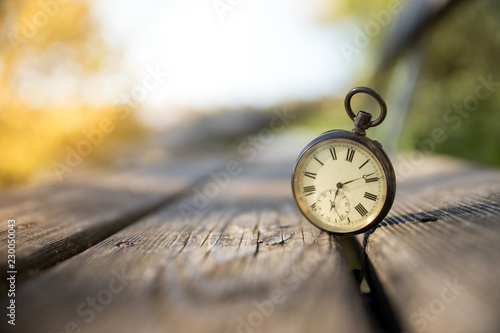 Retro Taschenuhr auf Holzbank, Himmel und bunte Blätter im Herbstlicht, Symbol für Zeit photo