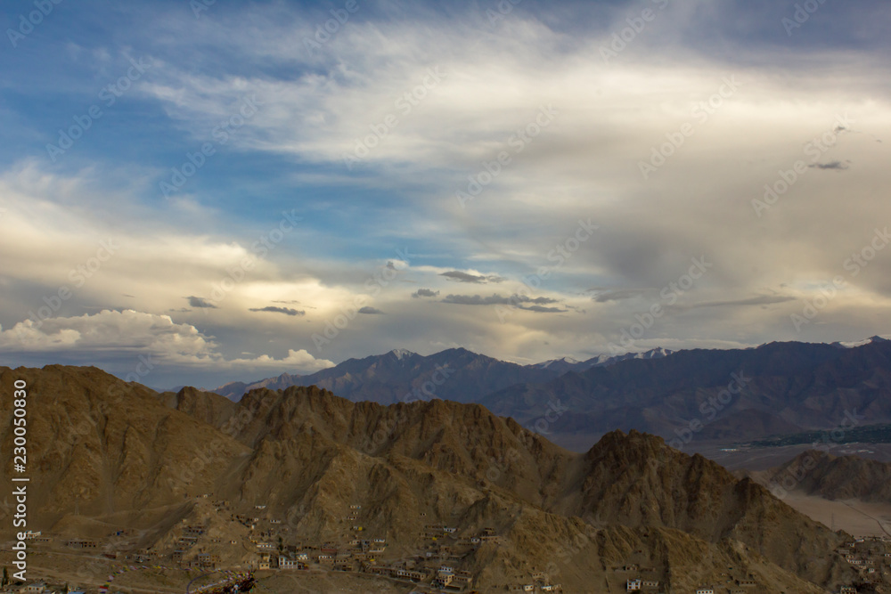 houses on the slopes of the desert mountains against the backdrop of snowy mountains under heavy sky
