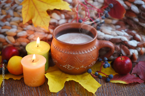 Cozy autumn composition with a cup of hot coffee, candles, fall leaves and scarf on a wooden background