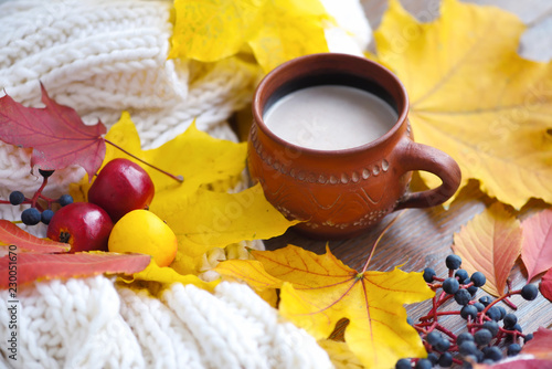 Autumn composition. Cup of coffee, colorful leaves and scarf on wooden background.
