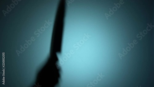 Killer slashing victim with a knife, spooky silhouette behind the glass, murder. Blood-chilling horror thriller shot