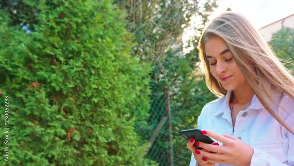 Woman texting on smartphone looking happy outside, Caucasian girl in her 20s happily texting on phone in public place, 4k Woman texting on smartphone looking happy outside, Caucasian girl in her 20s happily texting on phone in public place, 4k