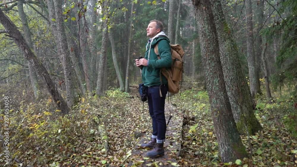 A middle-aged man with a backpack walks along an ecological natural educational trail through the northern autumn forest. Watching wildlife with binoculars in a nature park in Finland. Slow motion A middle-aged man with a backpack walks along an ecological natural educational trail through the northern autumn forest. Watching wildlife with binoculars in a nature park in Finland. Slow motion