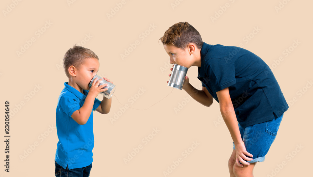 Two little brothers together talking through a tin phone on color baackground