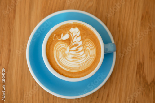 A cup of latte art coffee blue color mug ceramic swan shape beautiful foam on wooden table desk background.