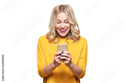Excited young woman looking at her mobile phone smiling. Woman reading text message on her phone, isolated over white background.