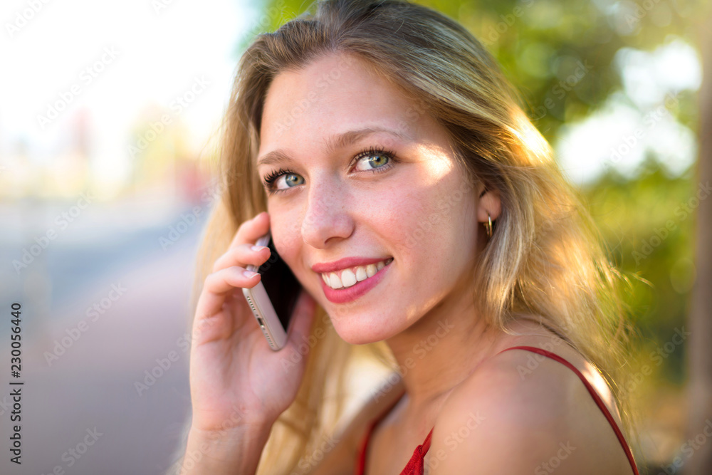 Young blonde girl keeping a conversation with the mobile phone with someone at outdoor Young blonde girl keeping a conversation with the mobile phone with someone at outdoor