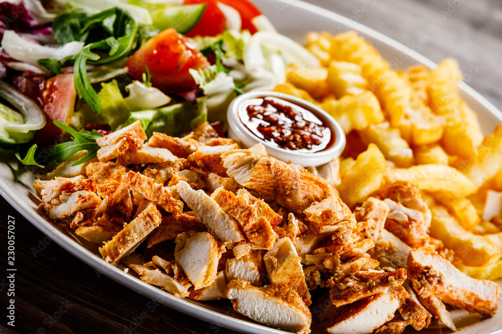 Kebab - grilled meat with french fries and vegetables on wooden background Kebab - grilled meat with french fries and vegetables on wooden background