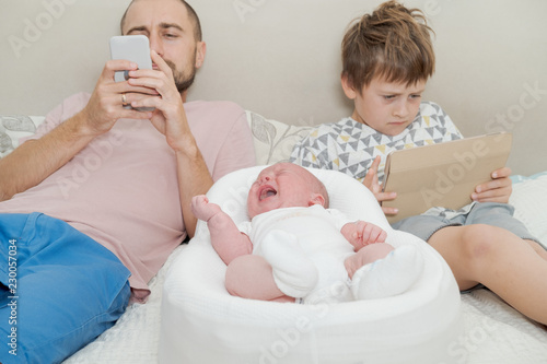 Internet addiction. Dad with son look into the phone near crying baby