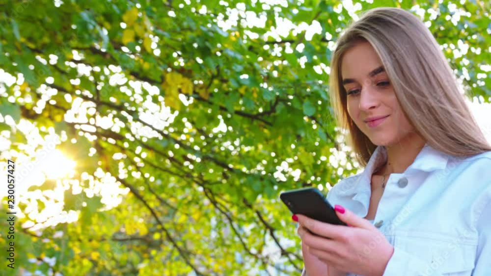 Woman texting on smartphone looking happy outside, Caucasian girl in her 20s happily texting on phone in public place, 4k Woman texting on smartphone looking happy outside, Caucasian girl in her 20s happily texting on phone in public place, 4k