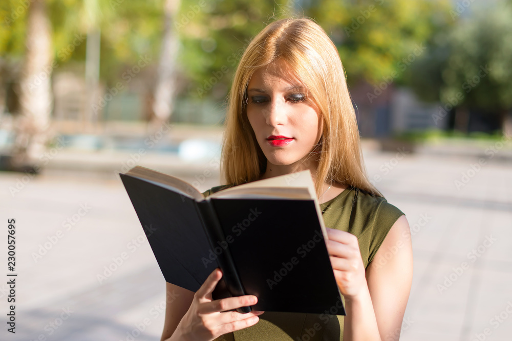 Obraz premium Pretty young teenager girl holding and reading a book at outdoors