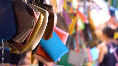 Handbags hanging from shop in busy market at night with out of focus people in background - Busy market scene photo