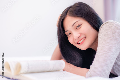 Pretty attractive Asian woman reading a fiction book, laying on the bed at bedroom 