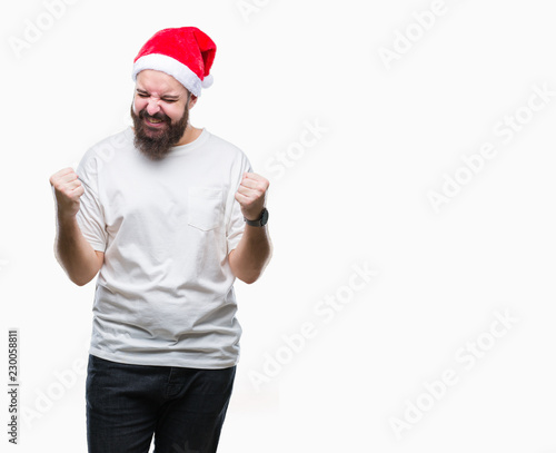 Young caucasian hipster man wearing christmas hat over isolated background very happy and excited doing winner gesture with arms raised, smiling and screaming for success. Celebration concept.