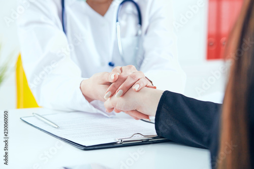 Friendly female doctor s hands holding female patient s hand for encouragement and empathy close-up. Partnership  trust and medical ethics concept.