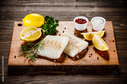 Fresh raw cod with herbs served on cutting board on wooden table