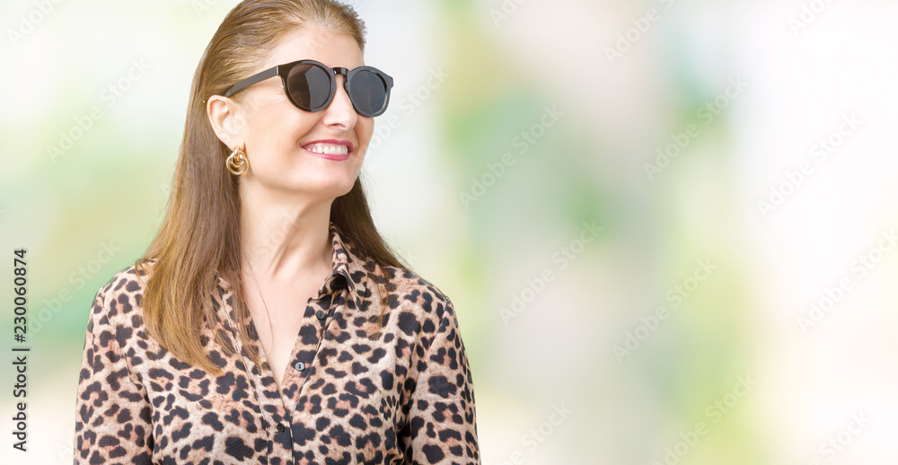 Middle age mature rich woman wearing sunglasses and leopard dress over isolated background looking away to side with smile on face, natural expression. Laughing confident. Middle age mature rich woman wearing sunglasses and leopard dress over isolated background looking away to side with smile on face, natural expression. Laughing confident.