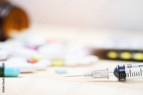 hypodermic syringe and Pill bottle spilling out. colorful pills capsule on to surface tablets on a table wooden background. drug medical healthcare surgery concept photo