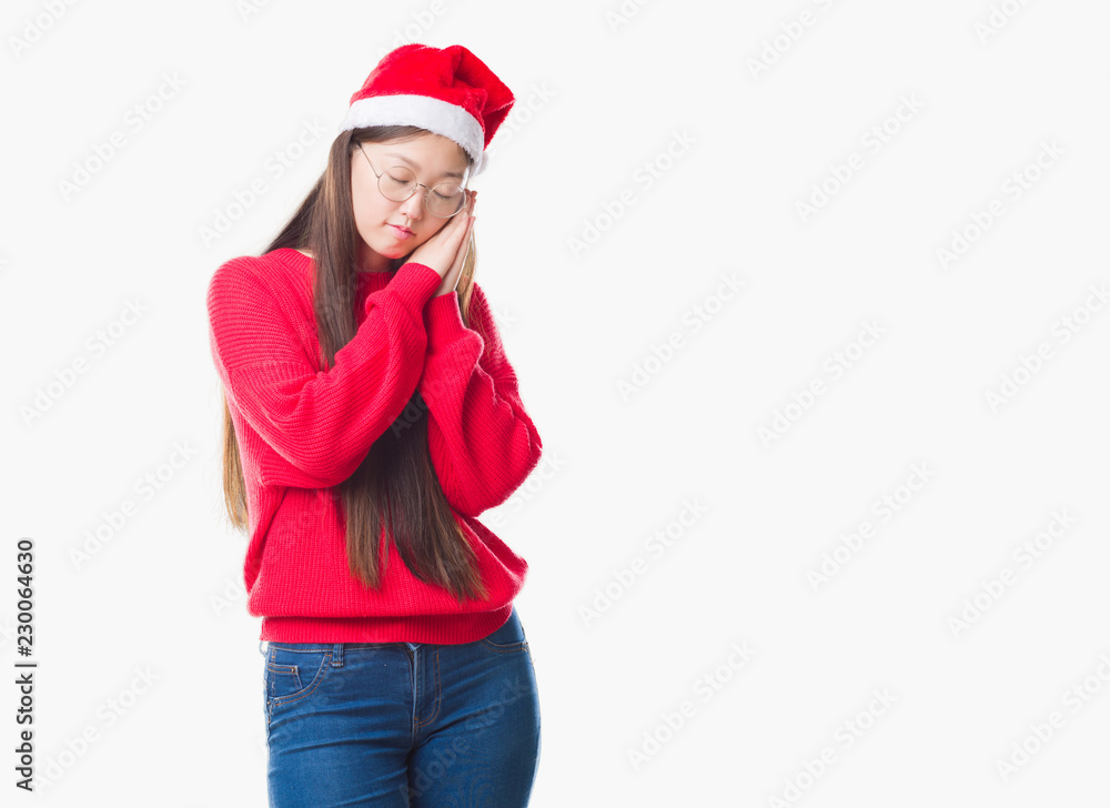 Young Chinese woman over isolated background wearing christmas hat sleeping tired dreaming and posing with hands together while smiling with closed eyes. Young Chinese woman over isolated background wearing christmas hat sleeping tired dreaming and posing with hands together while smiling with closed eyes.