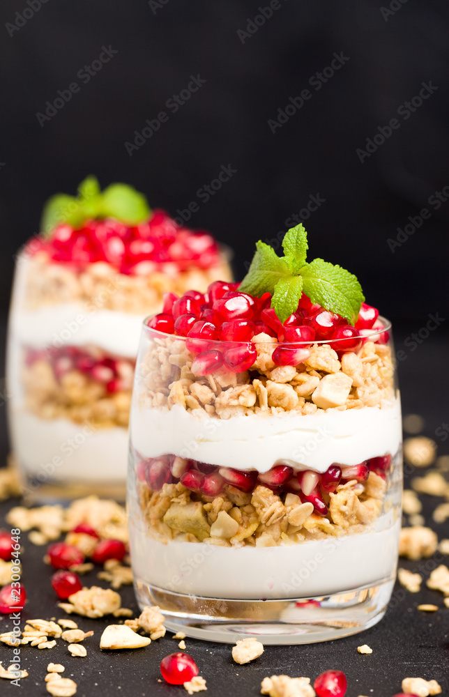 Pomegranate parfait - sweet organic layered dessert with granola flakes, yogurt and fruit seeds on black background. Pomegranate parfait - sweet organic layered dessert with granola flakes, yogurt and fruit seeds on black background.