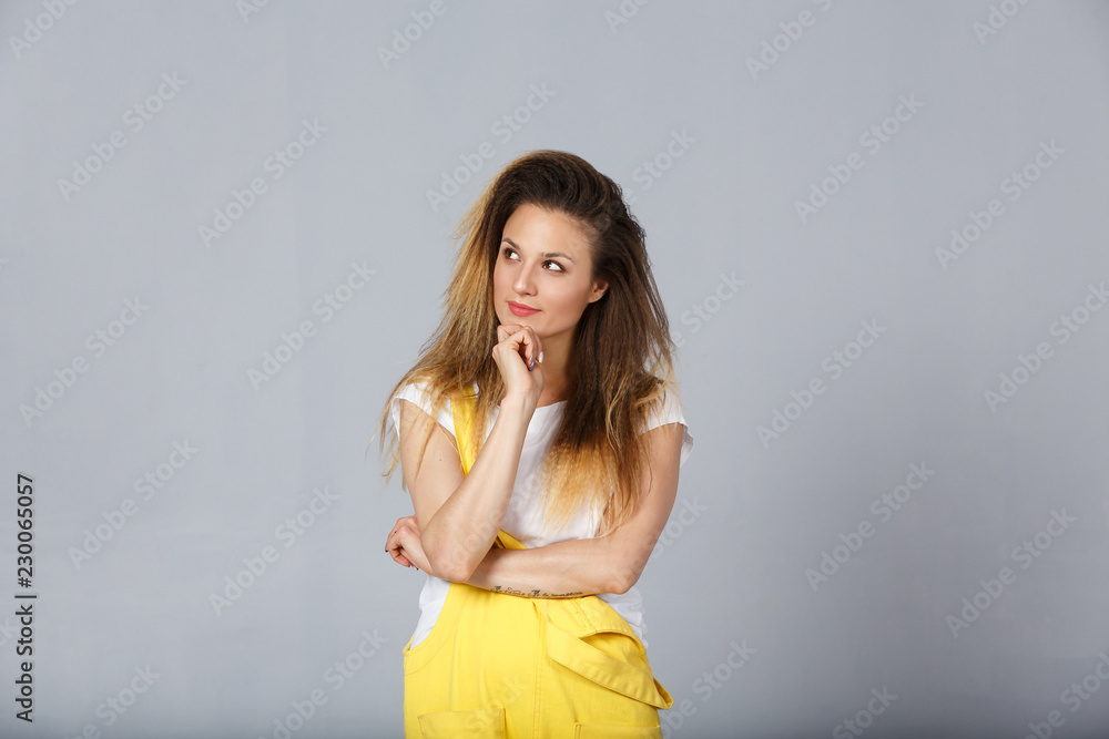 Portrait of good looking female adult wears stylish yellow overalls, holds chin and looks confidently at looking away, thinks about entering the university, chooses a specialty and future profession Portrait of good looking female adult wears stylish yellow overalls, holds chin and looks confidently at looking away, thinks about entering the university, chooses a specialty and future profession