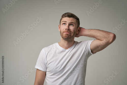 Attractive trendy young male freelancer with beard looking away with confused expression, scratching head, on isolated grey background. Handsome guy student remembers information for exam