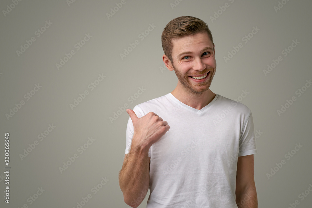 An unshaven man with blue eyes points his thumb at the copy space. A handsome guy shows something nice, smiles, advertises the goods An unshaven man with blue eyes points his thumb at the copy space. A handsome guy shows something nice, smiles, advertises the goods
