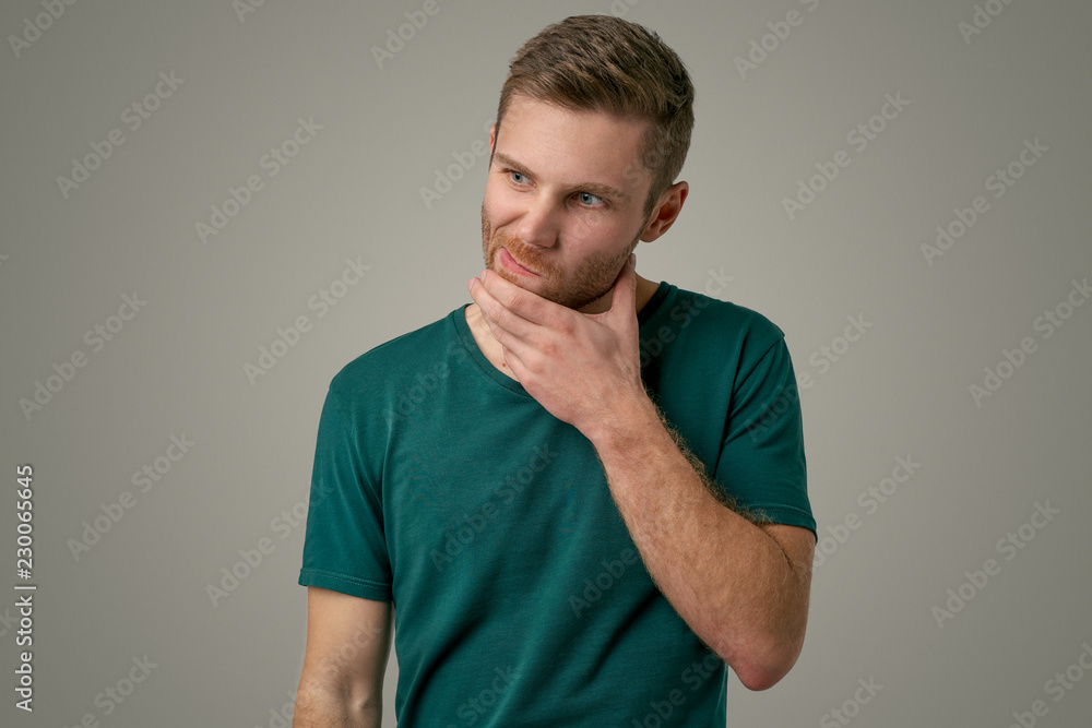 A handsome man holds his hand on chin, looks thoughtfully to the side, thinks about something important, tries to make decision. Man with bristles on grey background with copy space for promotional A handsome man holds his hand on chin, looks thoughtfully to the side, thinks about something important, tries to make decision. Man with bristles on grey background with copy space for promotional