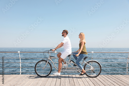 Couple riding tandem bike near sea on sunny day
